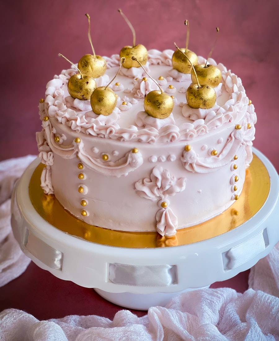 Torta rosada decorada con crema y cerezas doradas sobre un pie de torta